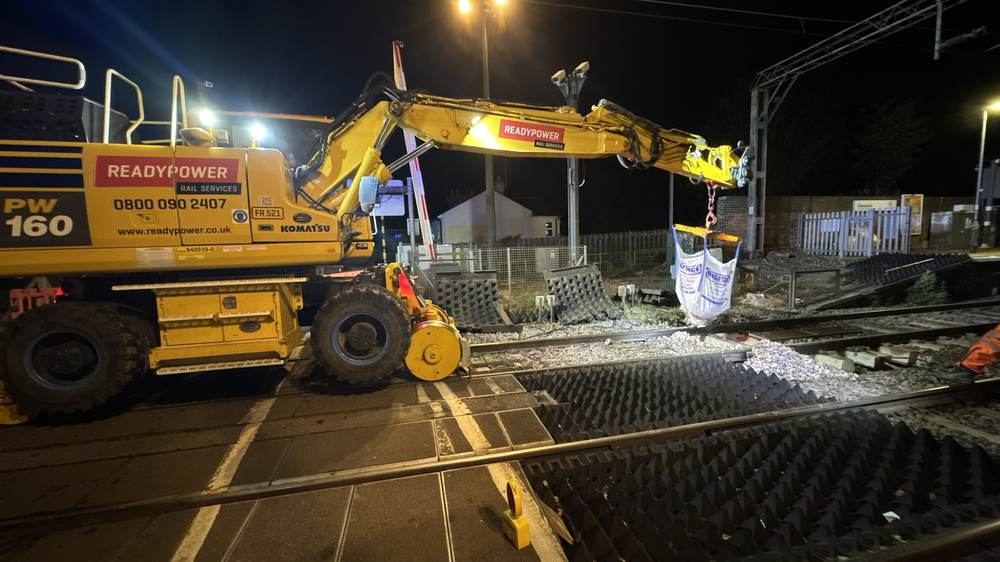 Road-rail excavator placing ballast bags during a night possession